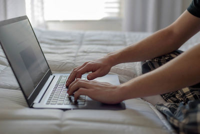 Cropped image of man using laptop on bed at home