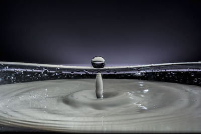 Close-up of drop falling on water against black background