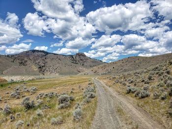 Dirt road leading towards mountains against sky