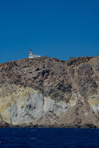 Lighthouse on cliff by sea against clear blue sky