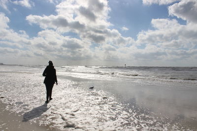 Rear view of man walking on beach against sky