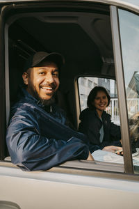 Portrait of smiling male delivery person sitting with female colleague in van