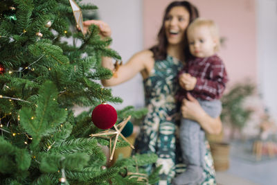 Cheerful mother carrying son at home with christmas tree in foreground