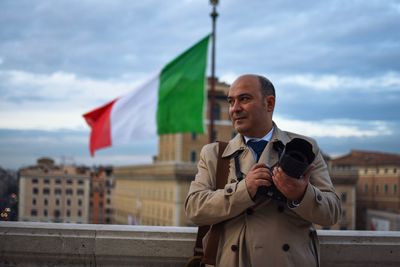 Mature man photographing while standing in city against sky
