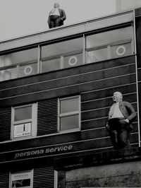 Low angle view of man sitting on window of building