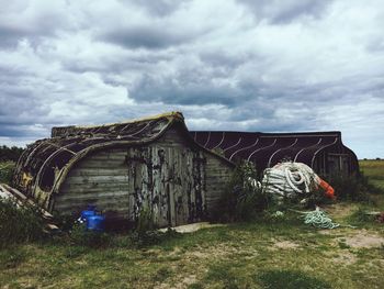 Abandoned wooden building in field against cloudy sky