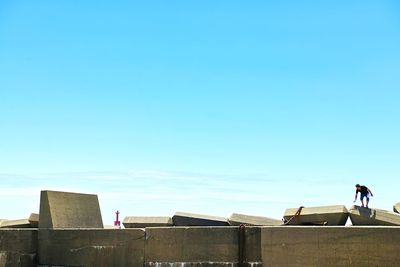 Man standing on retaining wall against clear blue sky