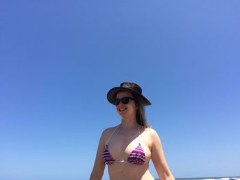 Low angle view of smiling woman wearing bikini standing against clear blue sky