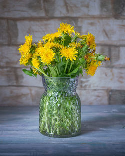 Bouquet of yellow dandelions with a glass vase on a wooden table in a rustic room