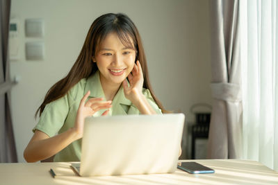 Portrait of smiling young woman using phone on table