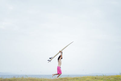 Carefree shirtless man carrying surfboard while running on meadow