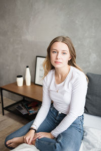 Beautiful young woman in bedroom looks thoughtfully at the camera.