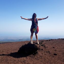 Rear view of woman standing on rock against sky