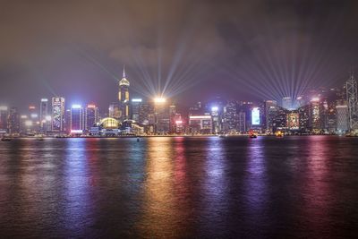 Illuminated buildings by river against sky at night