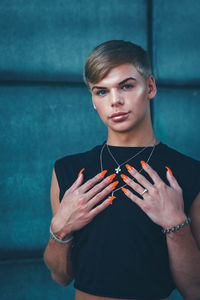 Portrait of young man holding camera while standing against wall