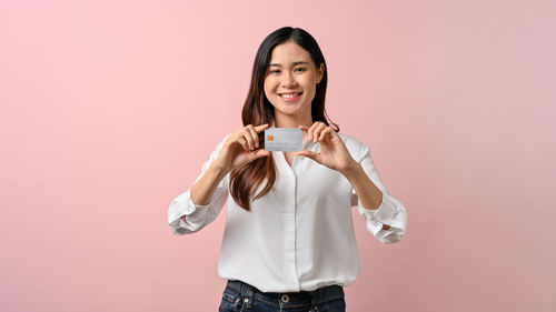 Portrait of young woman standing against pink background