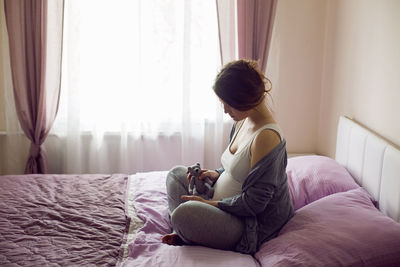 Pregnant young girl sitting on bed with teddy bear