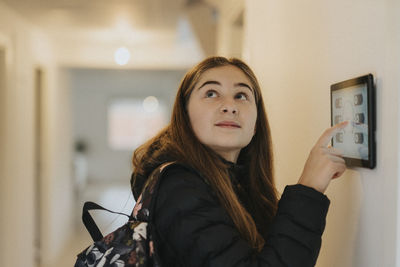 Side view of girl adjusting room lights through digital tablet mounted on wall at smart home