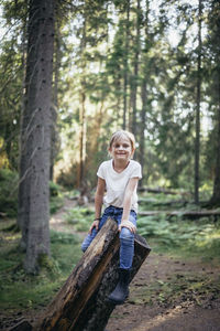 Portrait of smiling daughter sitting on log in forest