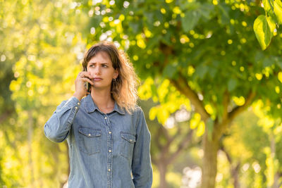 Young woman talking on phone against tree