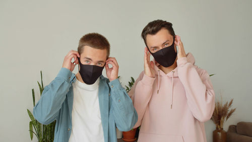 Portrait of gay couple wearing mask against wall