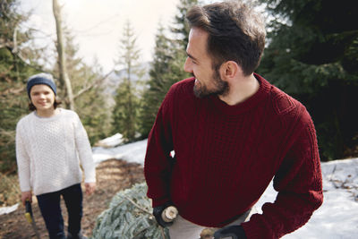 Father looking at teenage boy standing with hand saw in forest