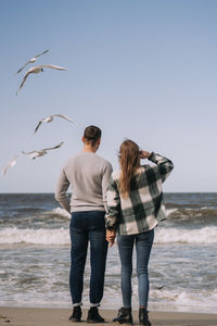 Rear view of couple on beach against clear sky