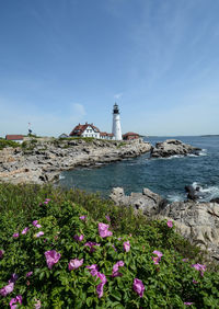 Lighthouse amidst sea and buildings against sky