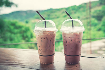 Close-up of iced coffee in disposable glasses on table against mountain