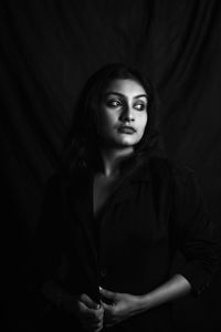 Portrait of young woman standing against black background