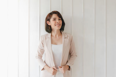 Portrait of smiling young woman standing against wall