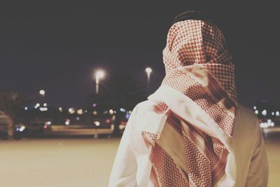 Rear view of man in traditional clothing on illuminated street in city at night