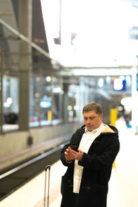 Man using mobile phone while standing at railroad station platform