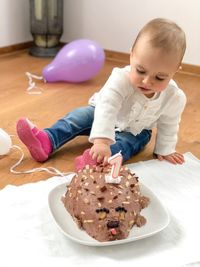 Cute girl touching birthday cake in plate on floor