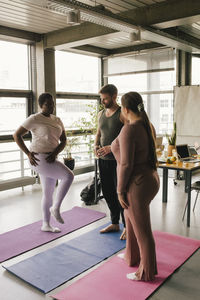 Full length of multiracial colleagues discussing while standing on mats at office