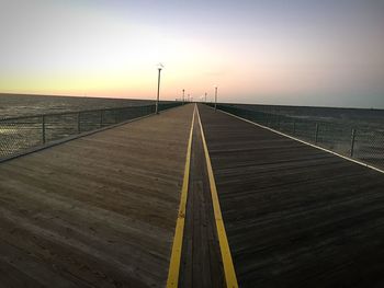 Long empty road by sea against sky during sunset