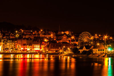 Illuminated city by river against sky at night