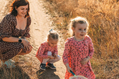 Mom and twin girls catch insects in outdoors with net and study nature with children