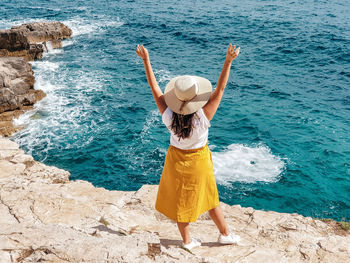 Rear view of woman standing on rock at sea shore