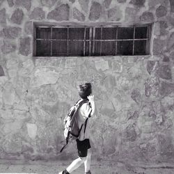 Rear view of young woman standing against brick wall