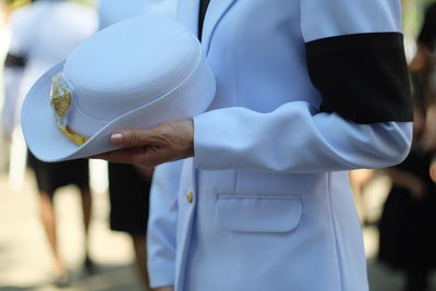 Midsection of man in suit holding hat while standing outdoors