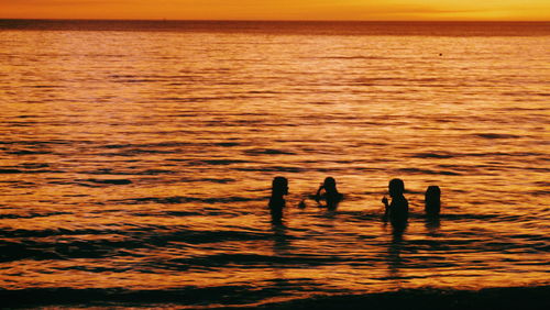 Silhouette people on sea against sky during sunset