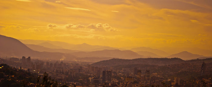 Panoramic view of cityscape and mountains against orange sky