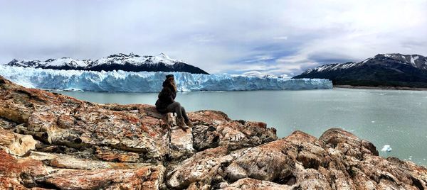 Mature woman wearing warm clothing while sitting on rock by sea during winter