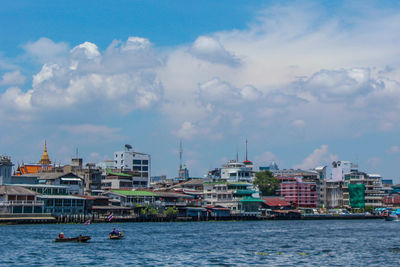 Sailboats in sea by buildings against sky