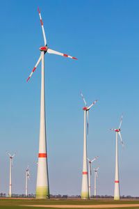 Low angle view of large windmills against clear blue sky