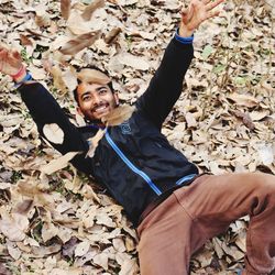 Smiling man lying down on land while playing with autumn leaf