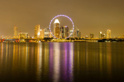 Singapore flyer by bay of water against sky in illuminated city at night