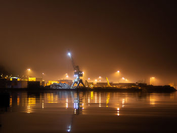 Illuminated city by river against sky at night