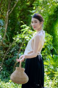 Portrait of young woman standing against trees